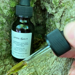 May include: A small amber glass bottle with a black dropper cap. The bottle is labelled "Lemon Balm" and lists the ingredients as Lemon Balm (Melissa officinalis), Alcohol (50%), and Water. The suggested use is to take 20-60 drops (1-3 droppers) up to 3 times a day. The bottle contains 1 fl oz / 30 ml.