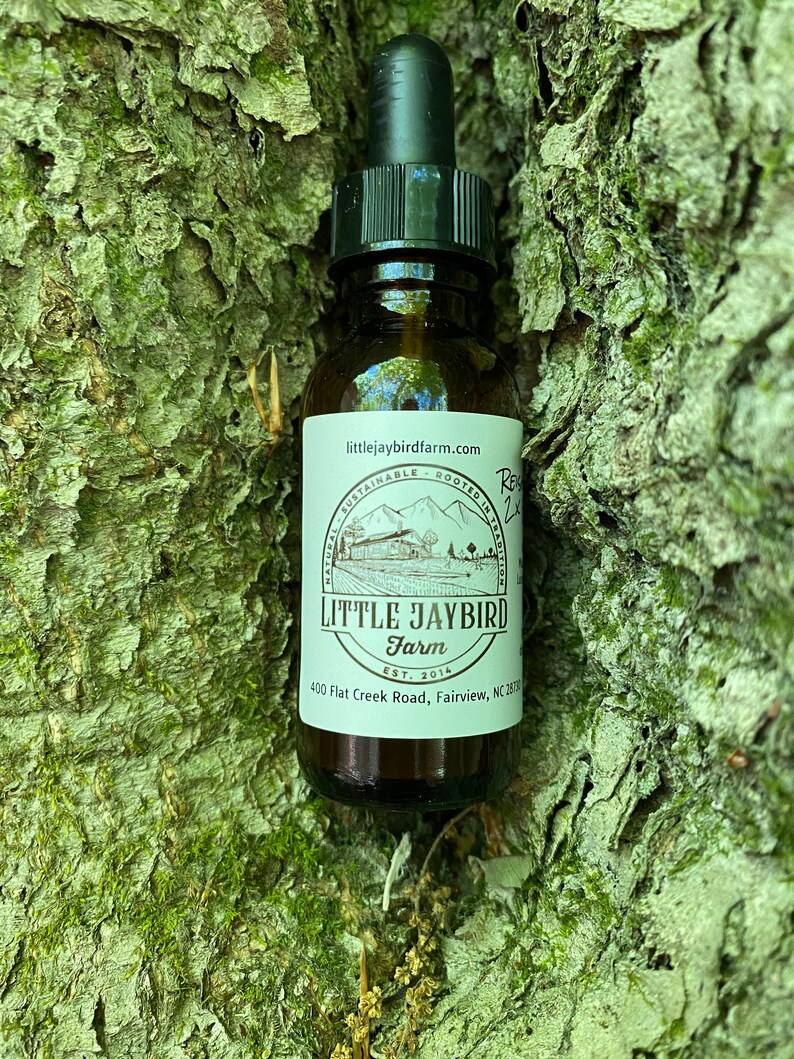 May include: A brown glass bottle with a dropper top and a white label. The label says "littlejaybirdfarm.com", "Naturally Sustainable - Rooted in Tradition", "LITTLE JAYBIRD Farm", "Est. 2014", and "400 Flat Creek Road, Fairview, NC 28730".