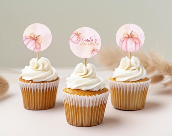 Może przedstawiać: Trzy babeczki z białym lukrem i dekoracyjnymi topperami. Toppery są okrągłe z akwarelowym wzorem dyni i napisem "Emily's Baby Shower". Babeczki są w białych papierowych papilotkach.
