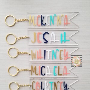 Peut inclure: Six porte-clés en acrylique transparent avec des chaînes dorées et des lettres colorées. Les noms McKenna, Jesa, Whitney, Micaela, Courtney et Alyssa sont inscrits sur les porte-clés.
