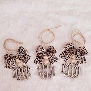 May include: Three wooden ornaments with leopard print bows and wooden beads. The ornaments are personalized with the letters "MBK", "SCM", and "KBD".
