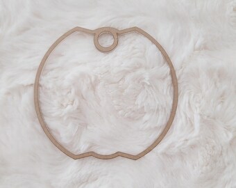 May include: A wooden apple-shaped ornament with a hole at the top for hanging. The ornament is light brown and has a smooth, polished finish.