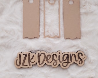 May include: Three unfinished wooden tags with rounded edges and a hole at the top. The tags are arranged in a row on a white fluffy surface. The text "JZK Designs" is visible below the tags.