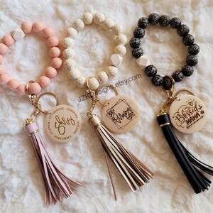 May include: Three beaded bracelets with wooden charms and tassels. The charms are engraved with the words "She is", "Mama", and "Blessed Mama".