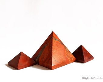 May include: Three red jasper pyramids of varying sizes, arranged in a row on a white background.
