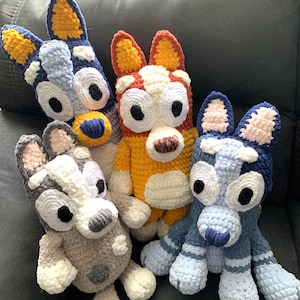 May include: Four crocheted stuffed toys resembling dogs from the cartoon series 'PAW Patrol'. The toys are in various colors, including blue, gray, orange, and white.