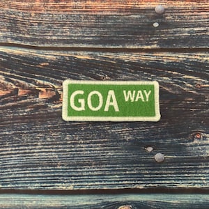 May include: A green and white sign with the text "GOA WAY" on a wooden background.