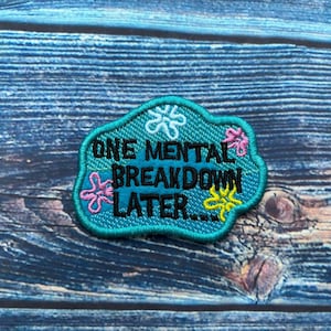 May include: A turquoise blue embroidered patch with a white, pink, and yellow flower design. The patch reads "One mental breakdown later..."