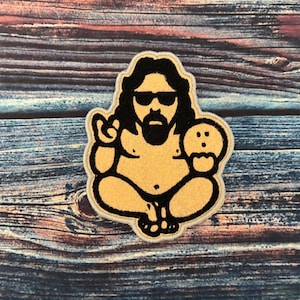May include: A black and yellow embroidered patch of a cartoon character with sunglasses, a beard, and a cookie in their hand. The character is sitting with their legs crossed and making a peace sign with their hand.
