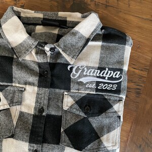 May include: Black and white plaid flannel shirt with a white embroidered patch that says "Grandpa est 2023".
