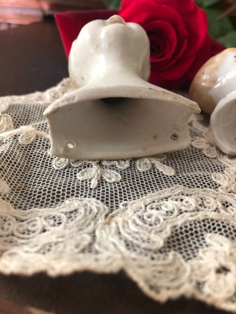 May include: Two vintage porcelain doll heads, one with a white finish and the other with a cream finish. Both heads are missing their bodies and have a hollow base.