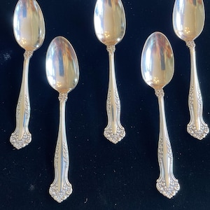 May include: Five silver spoons with ornate floral detailing on the handles and a reflective, oval bowl. The spoons are arranged against a dark background, showcasing their polished surfaces and intricate design. A classic silverware set.