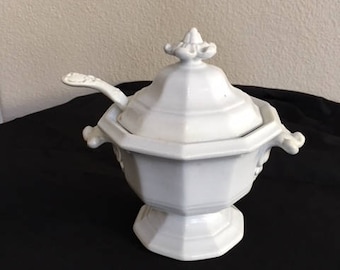 May include: White porcelain soup tureen with a lid and a matching ladle. The tureen has a fluted design and a decorative knob on the lid.