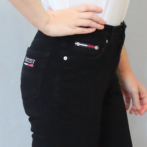 Puede incluir: Vaqueros negros de mezclilla con corte recto. Los vaqueros tienen el logo de Tommy Hilfiger en el bolsillo trasero y un peque&ntilde;o detalle del logo en el bolsillo delantero. El modelo lleva zapatos negros de punta abierta.