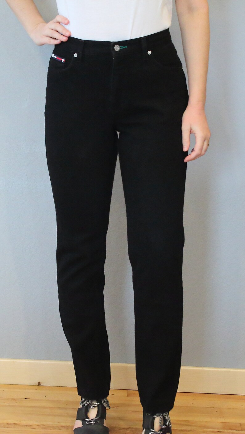 Puede incluir: Vaqueros negros de mezclilla con corte recto cl&aacute;sico. Los vaqueros tienen cierre de bot&oacute;n y cremallera, bolsillos delanteros y traseros, y un peque&ntilde;o detalle de logotipo en el bolsillo delantero. El modelo lleva una camiseta blanca.