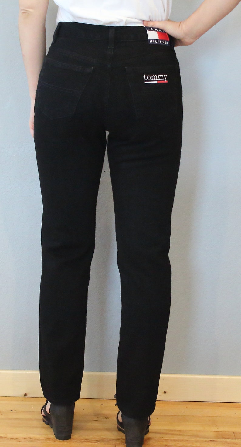 Puede incluir: Vaqueros negros de mezclilla con corte recto. La parte trasera tiene dos bolsillos y un parche con el logo de Tommy Hilfiger. Los vaqueros se llevan con sandalias de cu&ntilde;a negras. La modelo lleva un top blanco.