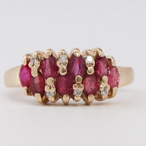 May include: A gold ring featuring a cluster of oval-cut, deep red gemstones, possibly rubies, accented with small, clear diamonds. The ring has a classic design with a polished gold band and a decorative setting for the gemstones.
