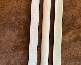 May include: Three wooden dowels, two are flat and one is round. The dowels are all the same length and are made of light wood.