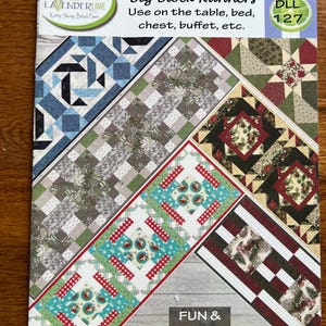 May include: A colorful book cover titled "Big Block Runners" featuring various quilt block designs in shades of blue, green, red, and brown. The cover includes text that reads "Use on the table, bed, chest, buffet, etc." and "FUN & FAST."
