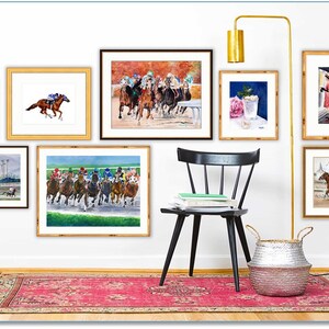 May include: A collection of framed watercolor paintings depicting horses racing, a cocktail, and a group of people. The paintings are hung on a white wall with a black chair and a silver basket in the foreground.