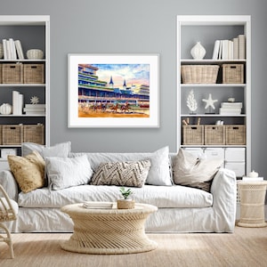 Pode incluir: Pintura em aquarela de uma corrida de cavalos em andamento, emoldurada em branco. A obra de arte retrata cavalos e j&oacute;queis correndo em uma pista, com arquibancadas e c&eacute;u azul ao fundo. A pintura &eacute; exibida acima de um sof&aacute; branco.