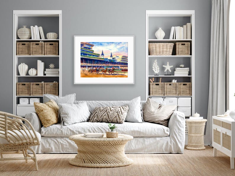Pode incluir: Pintura em aquarela de uma corrida de cavalos em andamento, emoldurada em branco. A obra de arte retrata cavalos e j&oacute;queis correndo em uma pista, com arquibancadas e c&eacute;u azul ao fundo. A pintura &eacute; exibida acima de um sof&aacute; branco.