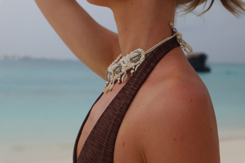K&ouml;nnte beinhalten: Nahaufnahme eines Frauenhalses, der eine wei&szlig;e und silberne Muschelkette tr&auml;gt. Die Kette hat ein geh&auml;keltes Design und verf&uuml;gt &uuml;ber kleine silberne Perlen und Muschelverzierungen.