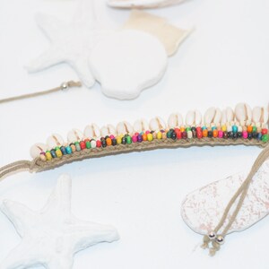 May include: A brown cord bracelet with white seashells and colourful beads. The bracelet is tied with a knot at the end.