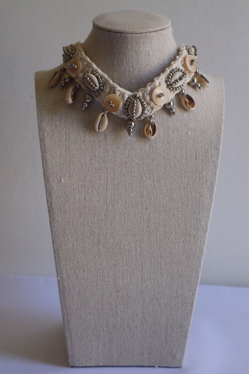 K&ouml;nnte beinhalten: Eine wei&szlig;e geh&auml;kelte Choker-Halskette mit silbernen Perlen und Muschelakzenten.