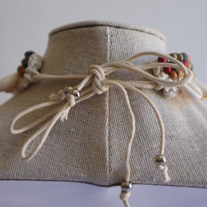 May include: A white and beige macrame necklace with colourful beads and shell accents. The necklace is tied with a simple knot and has silver metal beads on the ends of the cords.