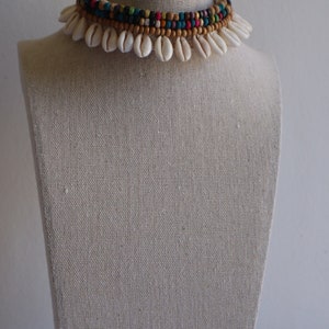 May include: A white shell choker necklace with a multi-coloured beaded layer. The beads are brown, black, blue, green, yellow, and red.