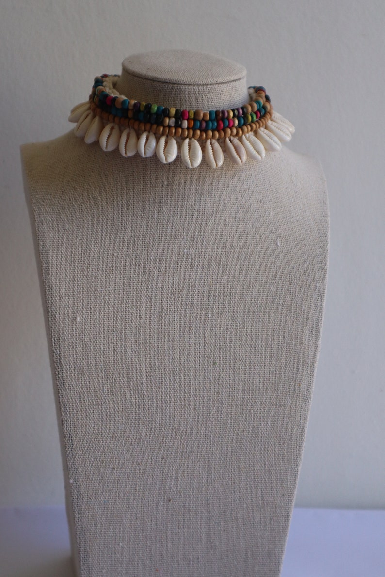May include: A white shell choker necklace with a multi-coloured beaded layer. The beads are brown, black, blue, green, yellow, and red.