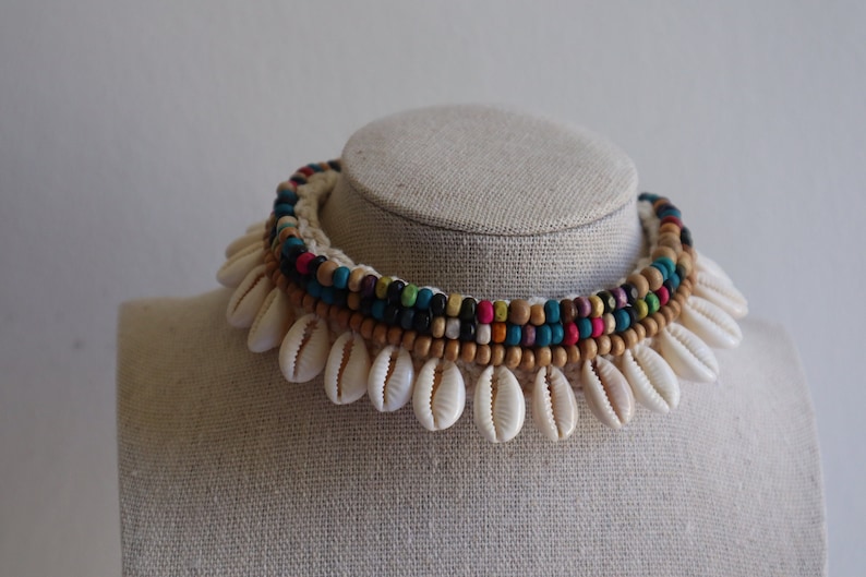 May include: A white shell necklace with a multi-coloured beaded strand. The beads are brown, blue, green, pink, and yellow.