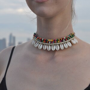 May include: A multi-layered necklace featuring white shell charms and colourful beads. The necklace is crafted from natural materials and has a bohemian style.