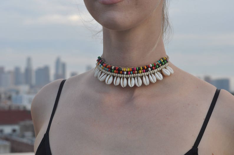 May include: A multi-layered necklace featuring white shell charms and colourful beads. The necklace is crafted from natural materials and has a bohemian style.