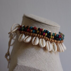 May include: A multi-strand anklet with wooden beads in brown, black, blue, green, red, and pink. The anklet is adorned with white seashells.