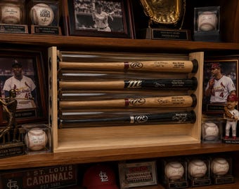 May include: A wooden display case holding four baseball bats in clear tubes. The bats are signed and displayed on a shelf with baseball memorabilia, including framed photos, baseballs, and a baseball glove.