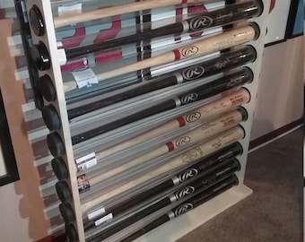 Peut inclure: Un présentoir à batte de baseball en bois blanc avec 12 tubes acryliques transparents contenant des battes de baseball signées. Les battes sont toutes en bois et ont un schéma de couleurs rouge, blanc et bleu. Le présentoir est sur un tapis brun.