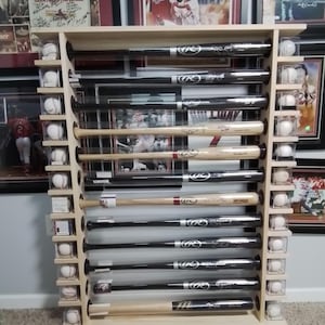 Könnte beinhalten: Ein Baseballschläger-Präsentationsständer aus Holz mit 10 durchsichtigen Acrylrohren, in denen signierte Baseballschläger aufbewahrt werden. Der Ständer hat 10 Regale mit Baseballbällen in jedem Regal. Der Ständer ist aus hellem Holz gefertigt und hat eine natürliche Oberfläche.
