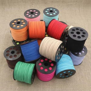 Peut inclure: Plusieurs bobines de cordon coloré, aux teintes variées : orange, rouge, bleu, vert, rose et noir. Chaque bobine est enroulée autour d'un noyau en plastique noir percé de multiples trous. Les cordons semblent être en matière douce, semblable à du daim.