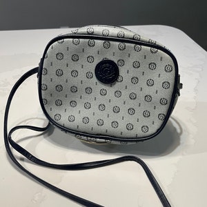 May include: A small, light blue and navy blue crossbody bag with a navy blue strap and a navy blue logo on the front.