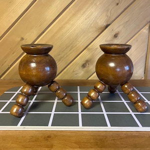 May include: A pair of wooden candle holders with a round base and three legs. Each leg is made of a series of small wooden beads.