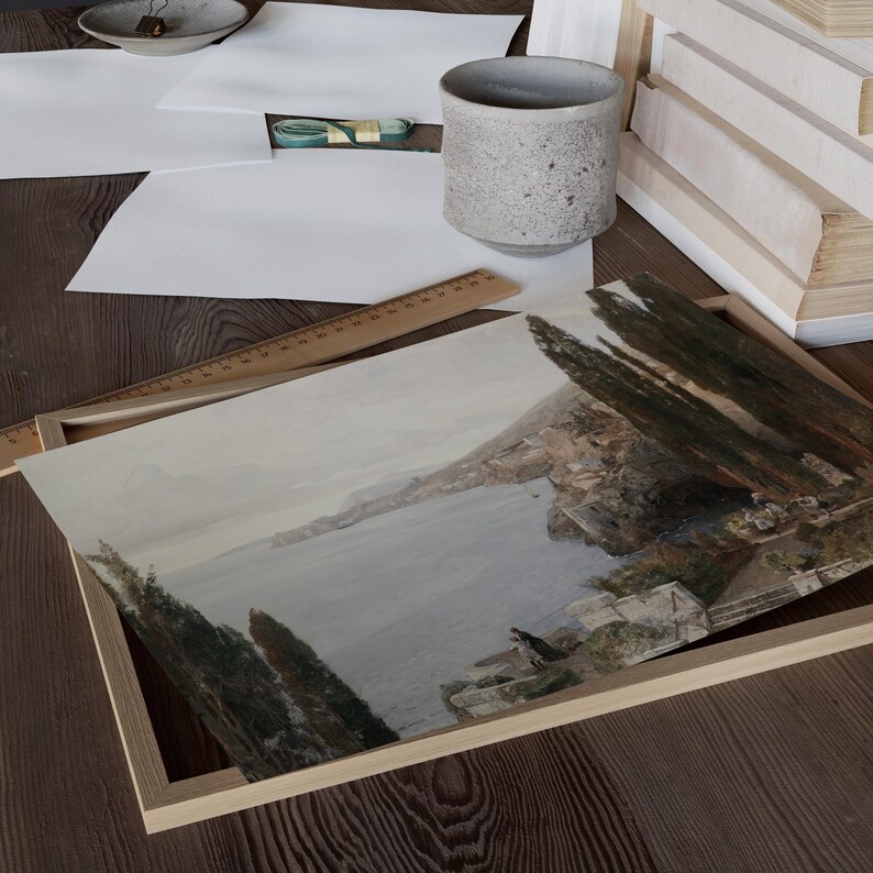 May include: A framed watercolor painting depicting a coastal scene with a town nestled on a hillside overlooking a calm blue sea. Lush green trees line the hillside and the water's edge.