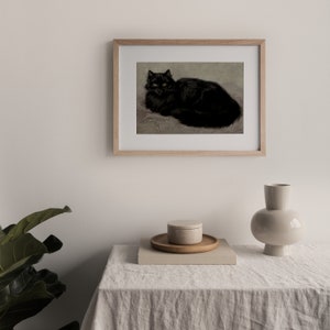 Pode incluir: Uma impress&atilde;o emoldurada em preto e branco de um gato preto com olhos amarelos deitado em uma superf&iacute;cie texturizada. A moldura &eacute; de madeira clara.