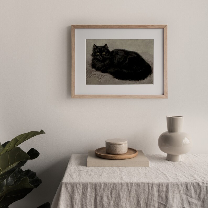 Pode incluir: Uma impress&atilde;o emoldurada em preto e branco de um gato preto com olhos amarelos deitado em uma superf&iacute;cie texturizada. A moldura &eacute; de madeira clara.