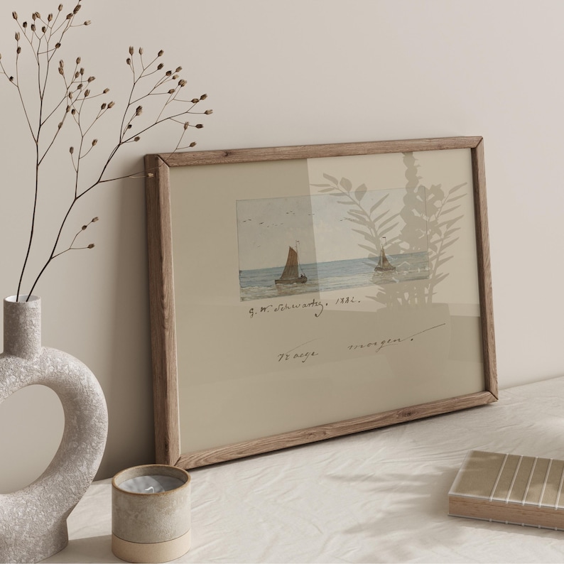Puede incluir: Una impresi&oacute;n en acuarela enmarcada de veleros en el mar. La obra de arte tiene un marco de madera clara y presenta texto escrito a mano. Un jarr&oacute;n con ramas secas y una vela est&aacute;n en primer plano.