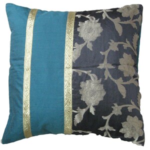 May include: Square decorative pillow with a teal blue panel and a dark blue floral patterned panel. Gold trim borders the teal panel. The pillow is a square shape and appears to be made of a soft fabric.