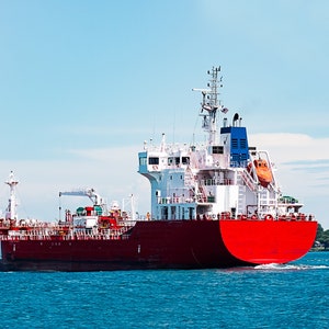 Może przedstawiać: Czerwono-biały tankowiec z niebiesko-białą nadbudówką płynie po niebieskiej wodzie. Statek ma łódź ratunkową po prawej burcie.