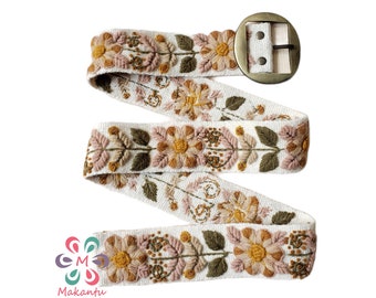 Peut inclure: Une ceinture en tissu blanc avec un motif floral brodé dans des tons de brun, rose et jaune. La ceinture a une boucle en laiton.