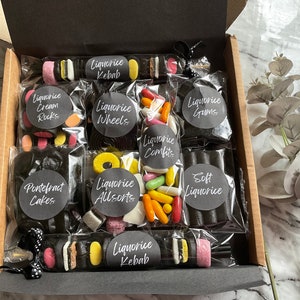 May include: A gift box filled with a selection of licorice sweets, including licorice kebabs, cream rocks, wheels, allsorts, comfits, and soft licorice. The box is lined with black paper and the sweets are packaged in clear plastic bags with black labels.